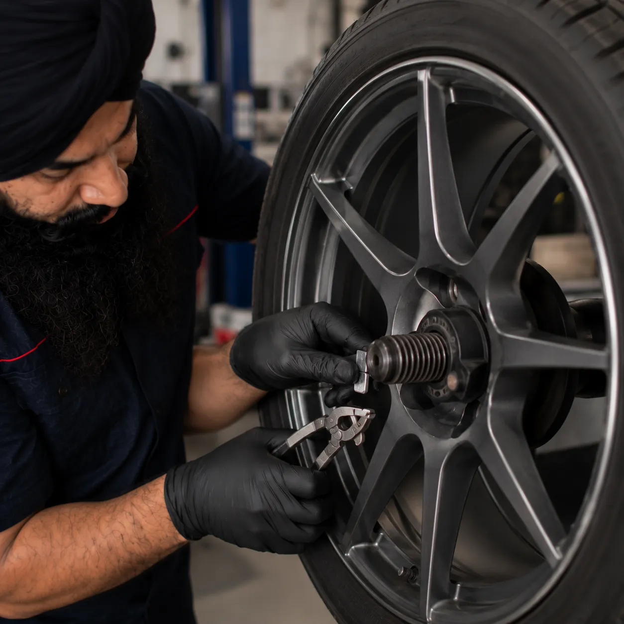 Mechanic fitting a balancing counterweight to a wheel rim in Beenleigh